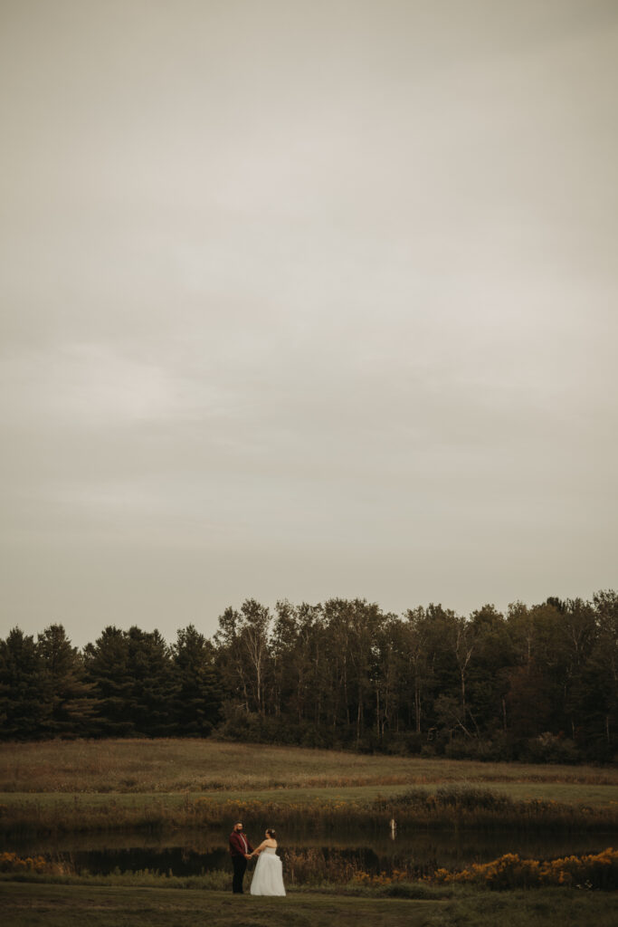 A couple elopes at the base of a lake in a beautifully wooded national park.