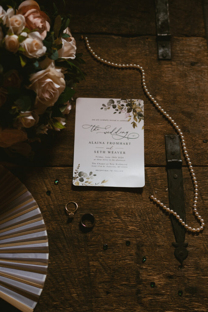 A flat lay with the bride's jewelry, the couples rings, and their wedding invitation.