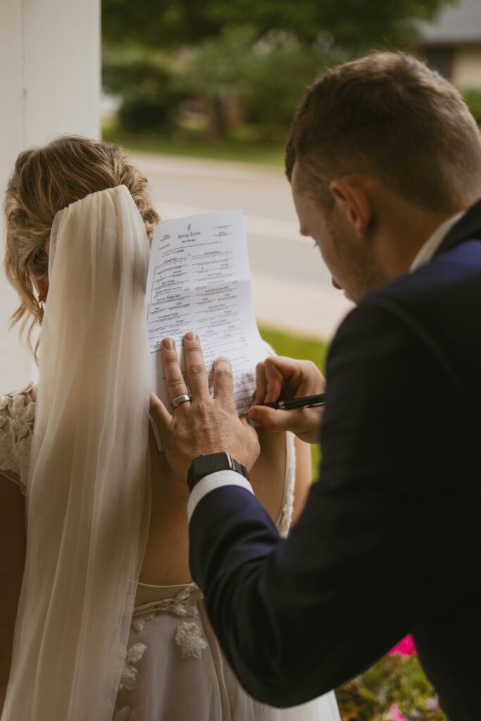 A groom signs his marriage license on his new wife's back in front of the church they got married in. 