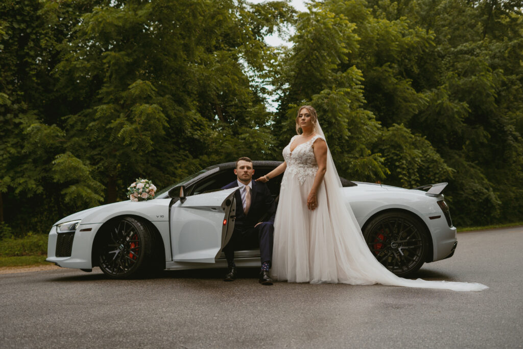 Married couple stands in front of sportscar that they used as their getaway car.