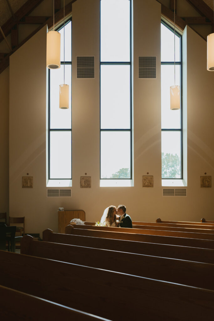 bride and groom sit in the sun kissed pews of their church