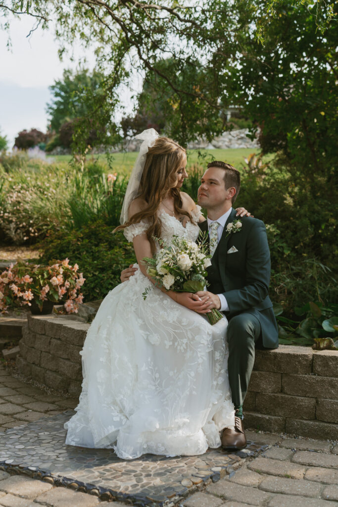 bride sits on grooms lap by a pond