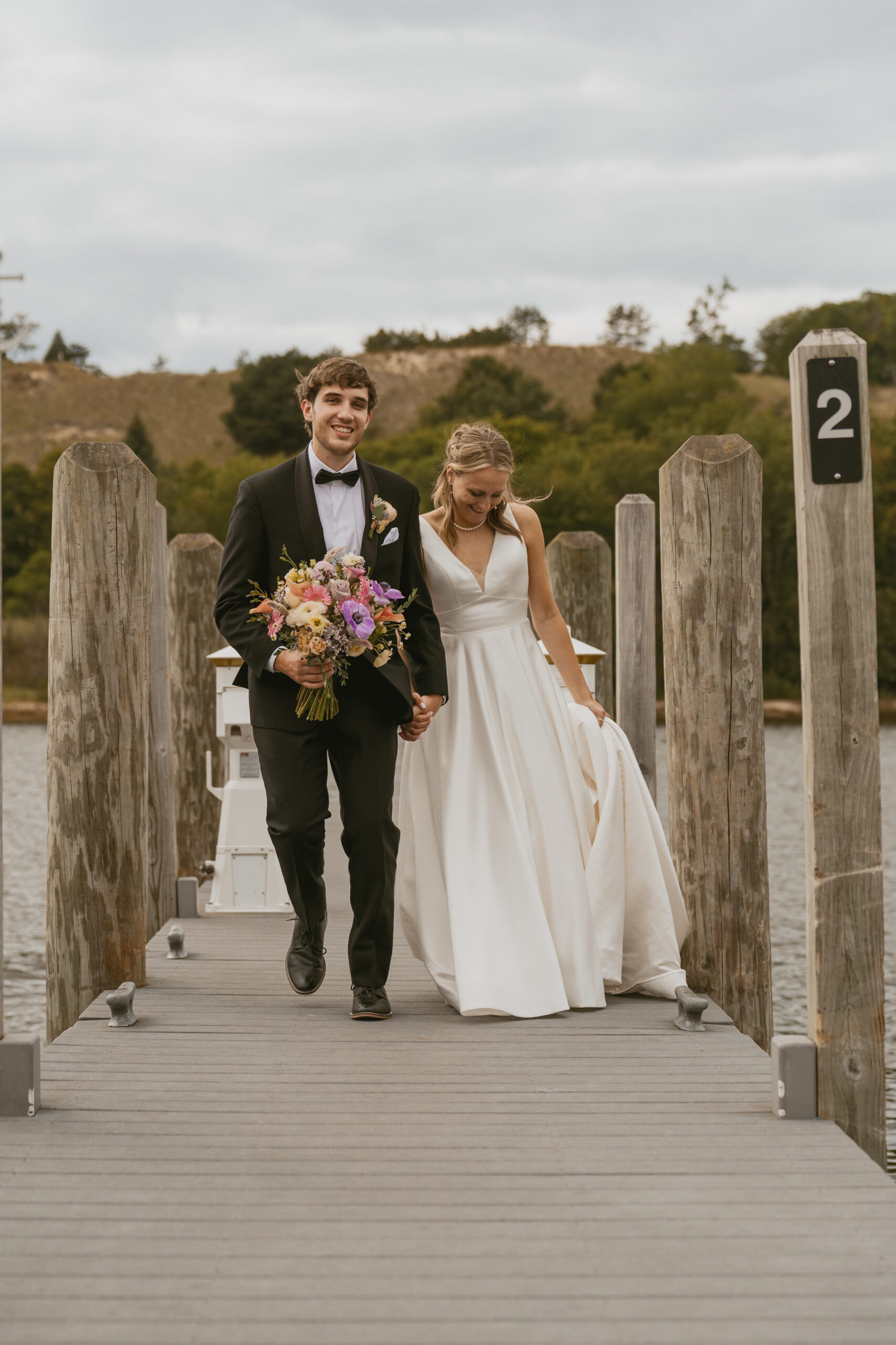 Bride and Groom holding bouquet walking down the boardwalk by the water.