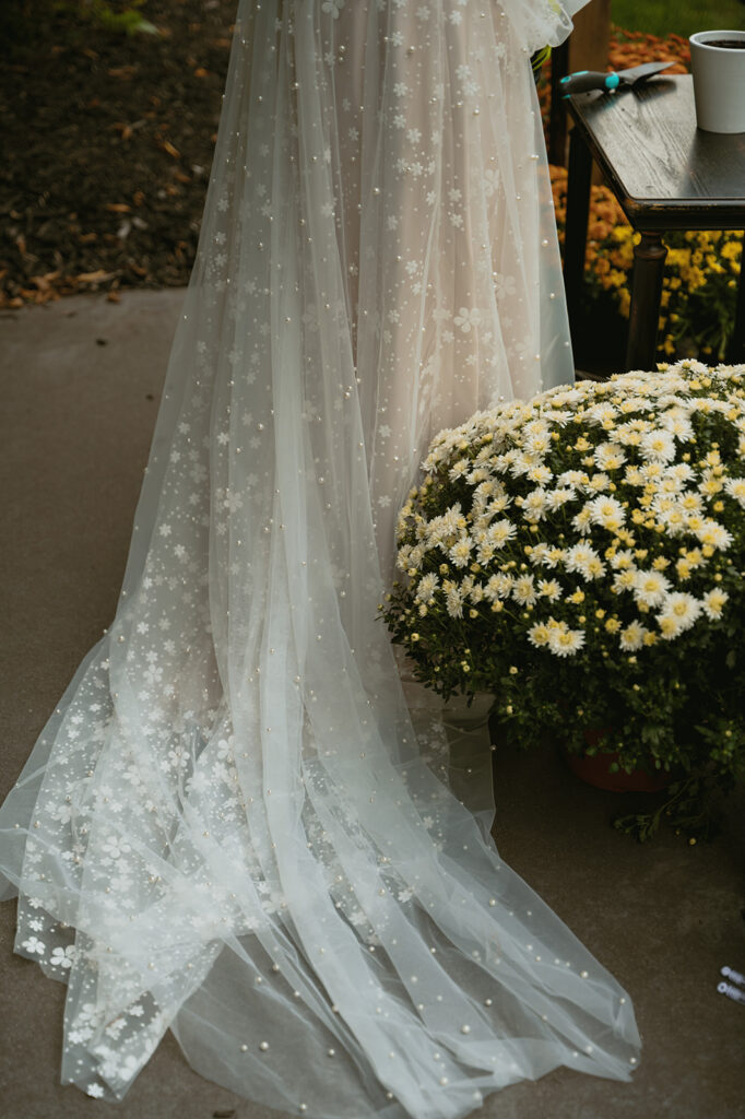 beautiful brides wedding dress hangs beside beautiful flowers