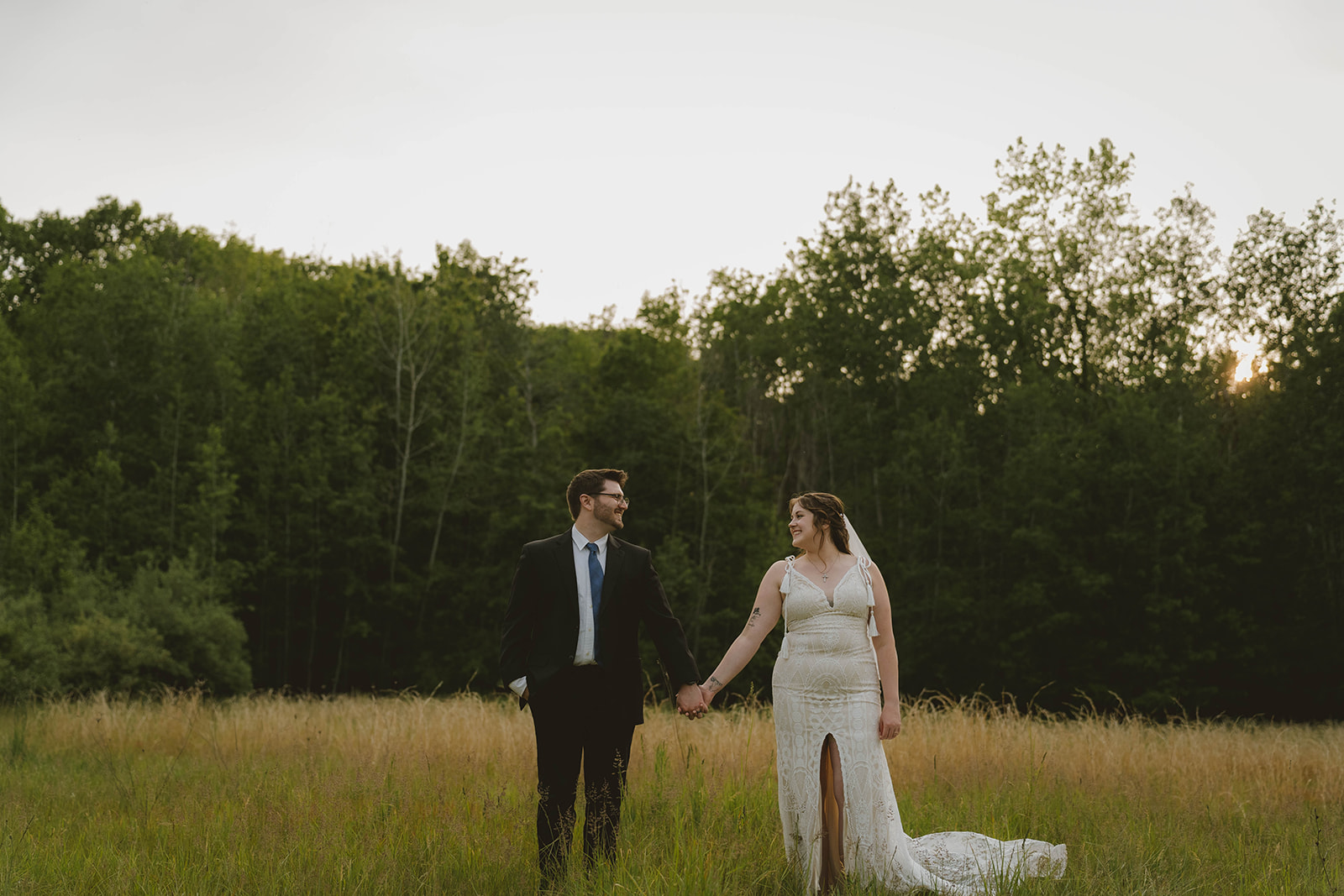 bride and groom smile at each other as they pose hand in hand in the Michigan wilderness