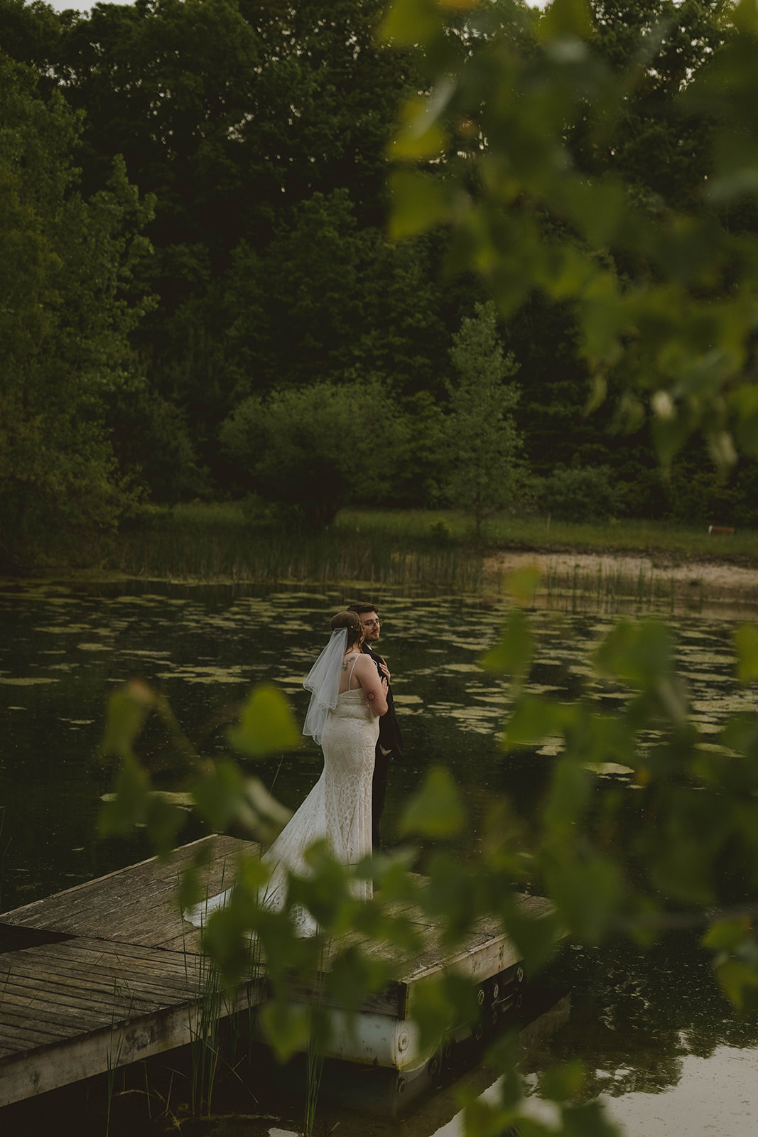 bride and groom pose on the end of a dock after their backyard wedding
