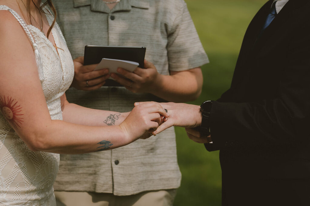 bride slides the ring on her new husbands finger as they finish their backyard wedding ceremony