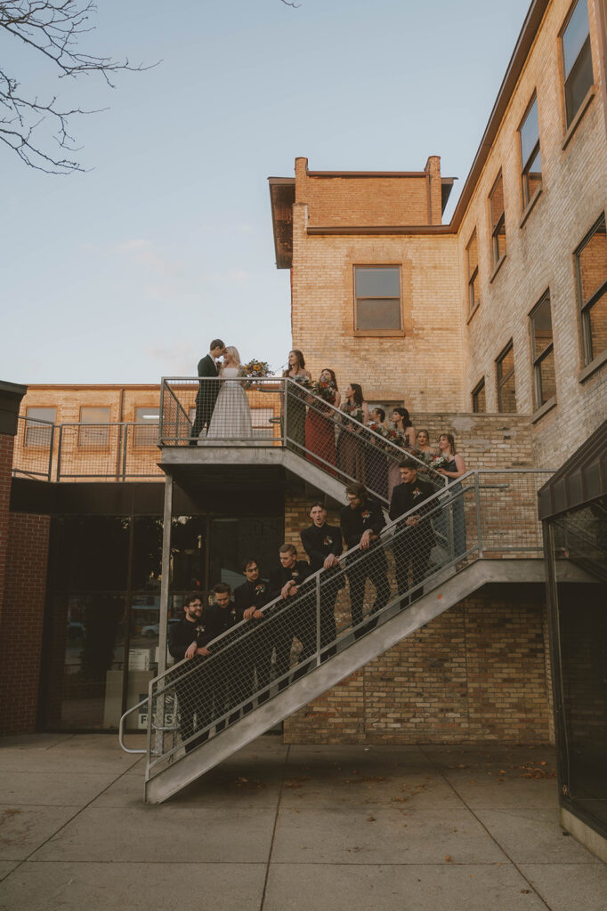 wedding party pose for a photo on the stairs outside the stunning wedding venue in Michigan