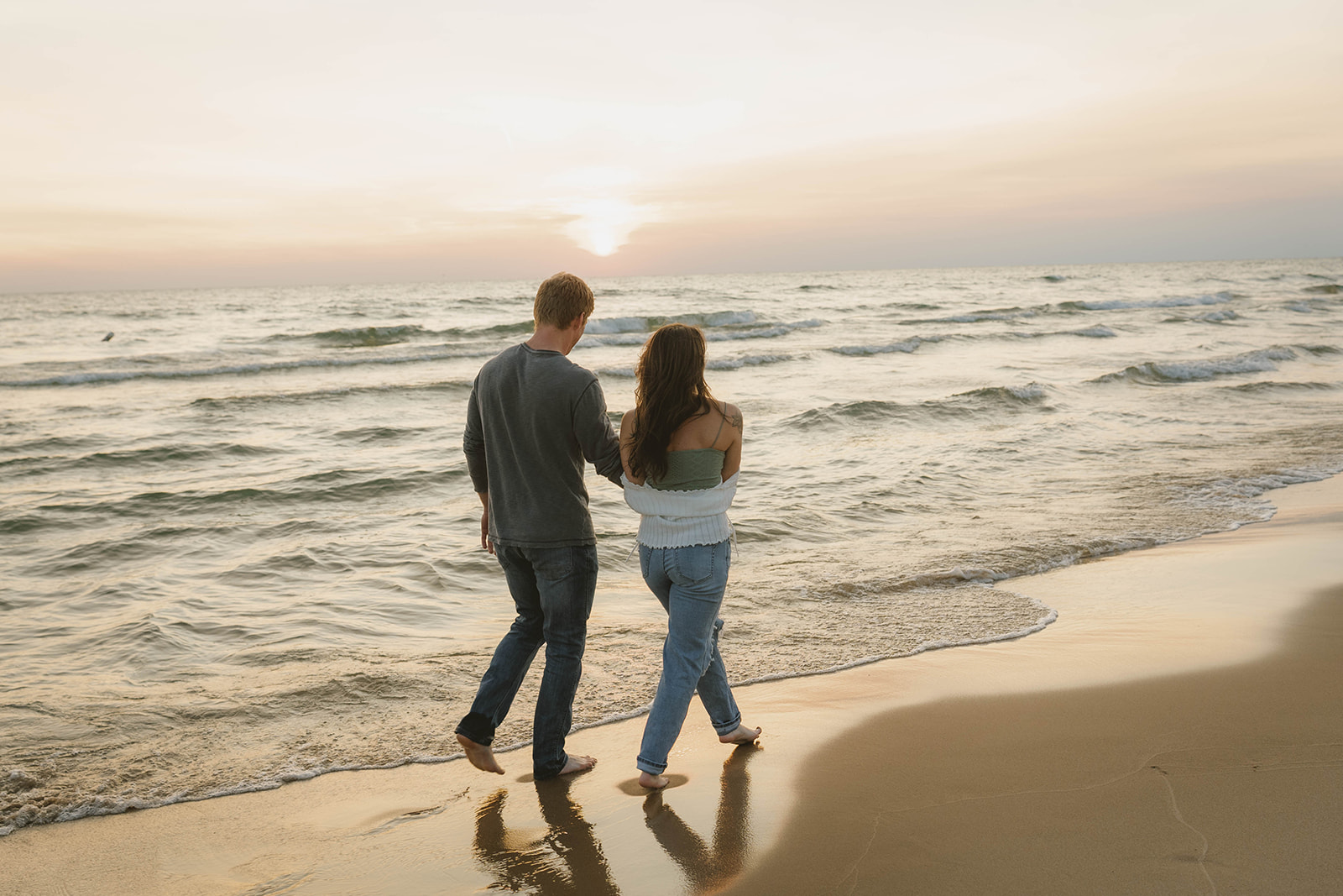 stunning couple walk on the beach during golden hour at their beach engagement pictures on Lake Michigan