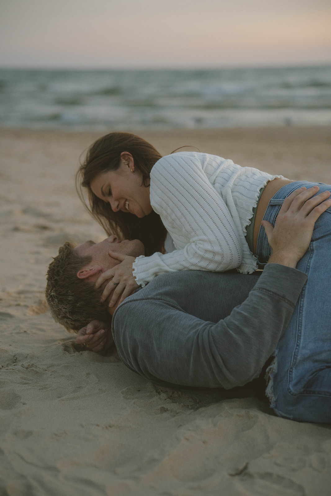 couple share an intimate moment lying on the beach together during their Michigan engagement session