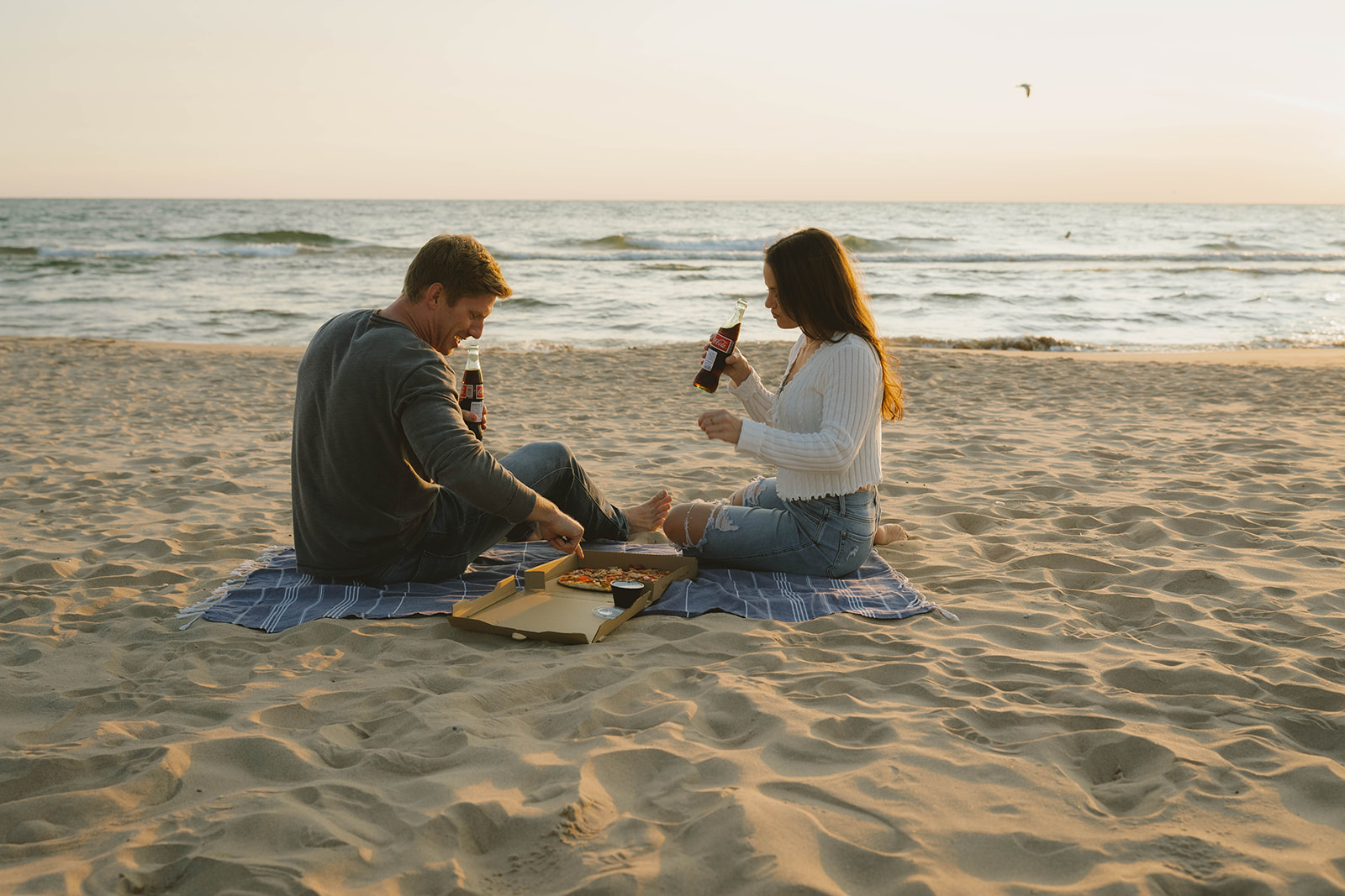 couple share a pizza and coke during their Lake Michigan engagement photos