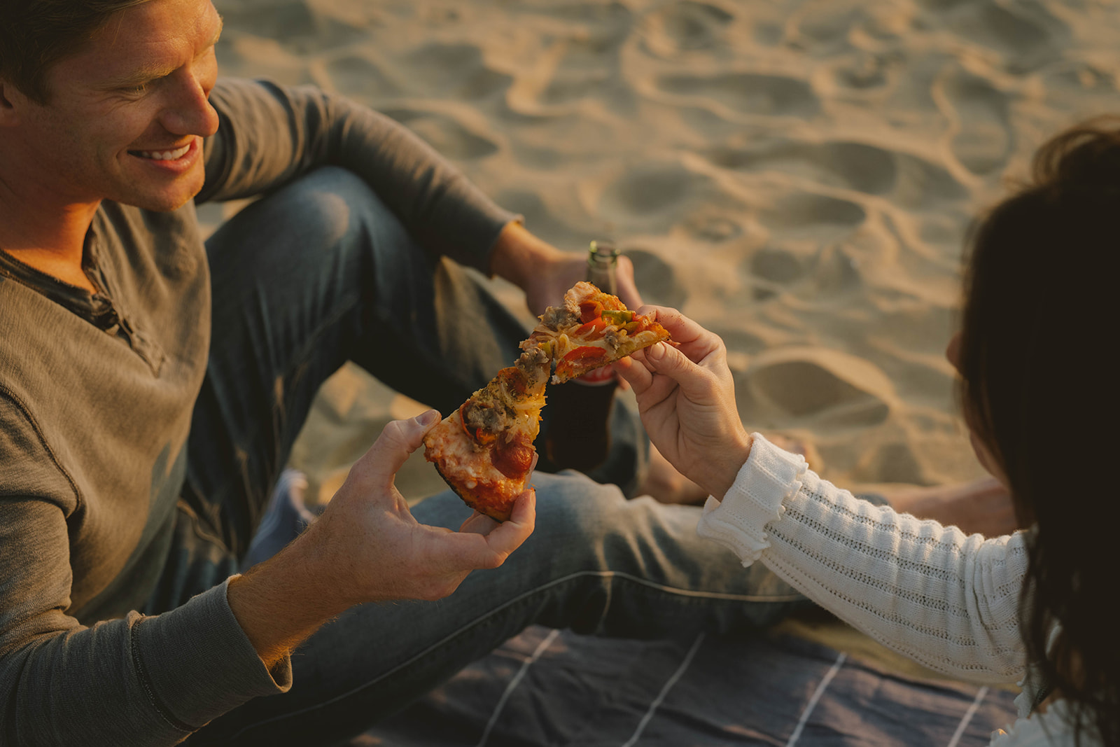 couple laugh and enjoy pizza on the beach