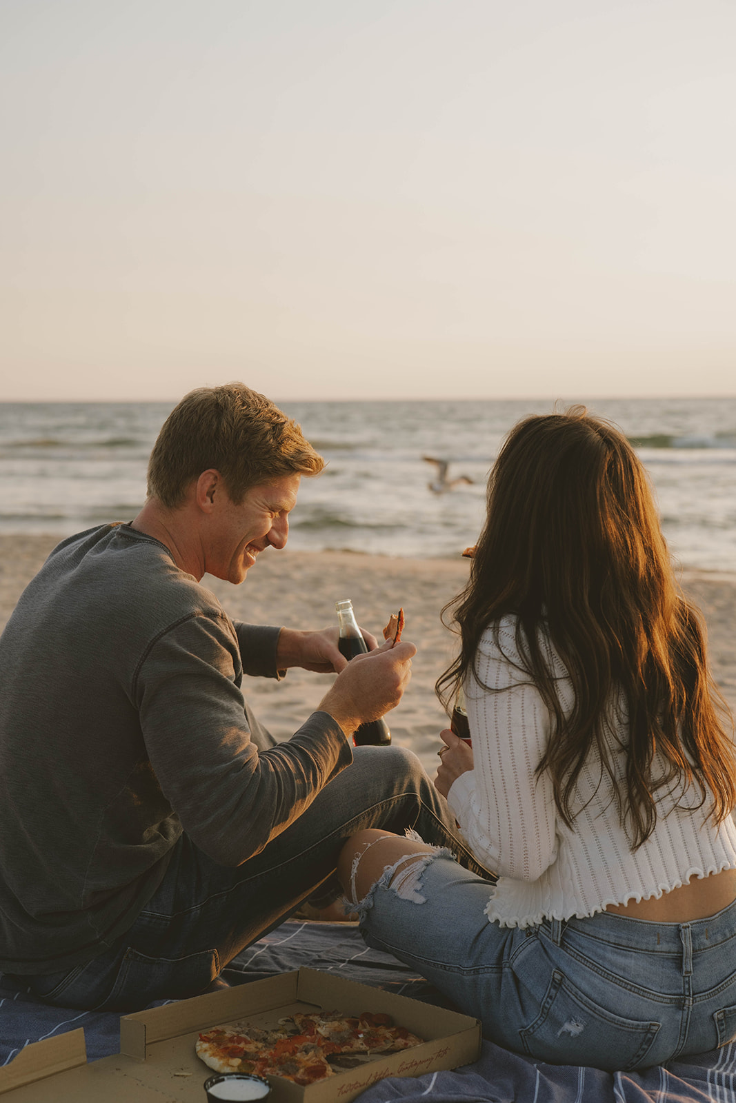 couple laugh and enjoy pizza on the beach