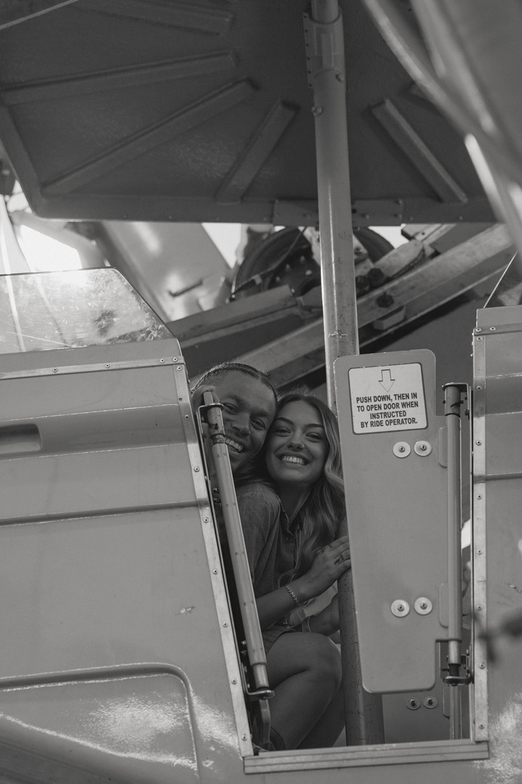 couple share laughter and smile at the camera together as they get ready in the seat of the ferris wheel
