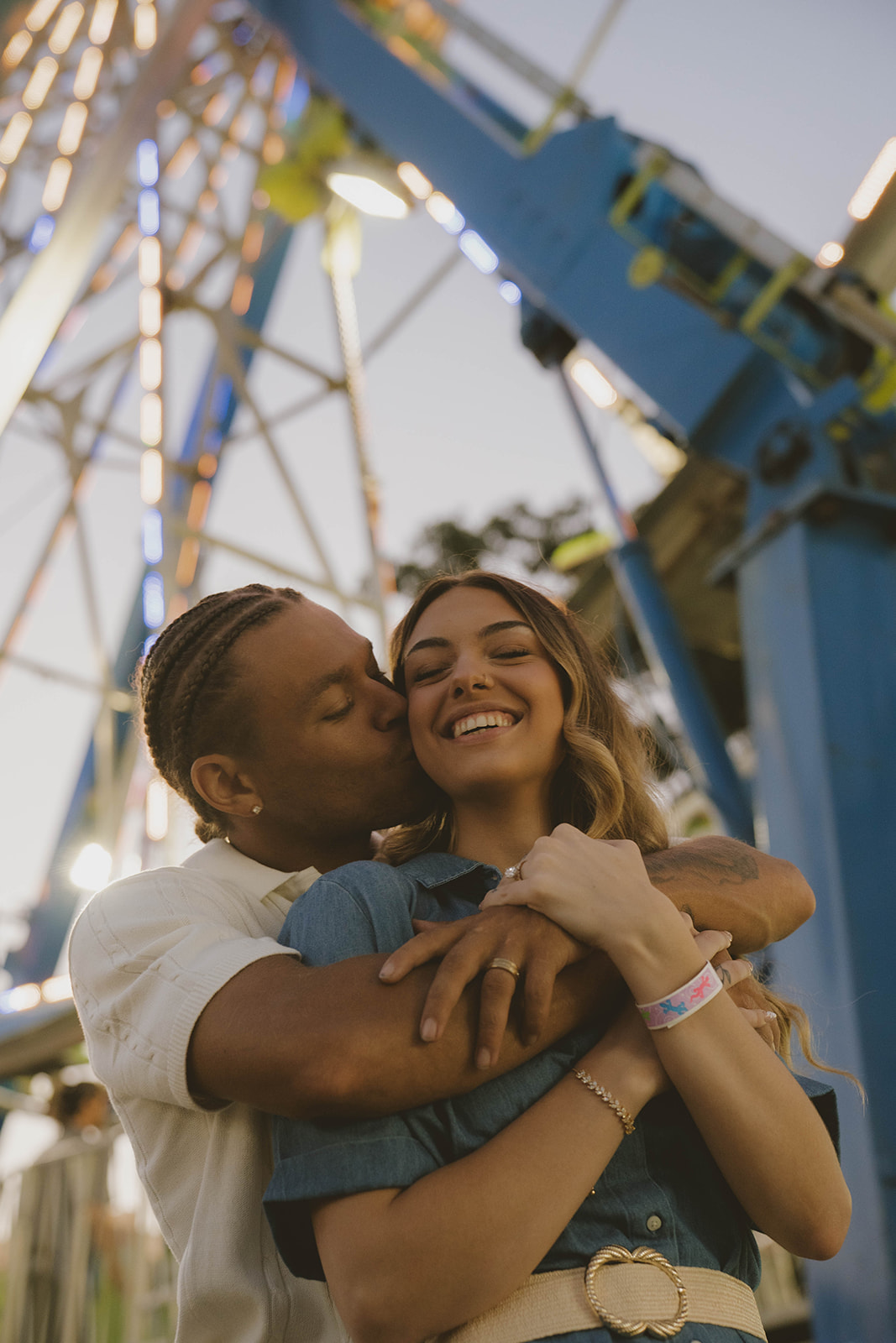 couple share a kiss on the cheek under the state fair ferris wheel